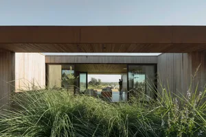 A modern house with large glass windows showing an indoor living space.