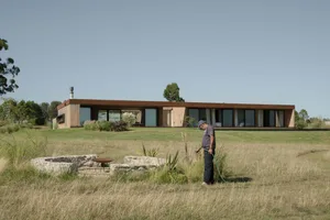 Man watering lawn on a sunny day in front of a modern residential exterior with a metal roof and metal roof vent.