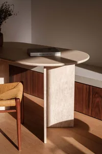 A minimalistic concrete desk with a wooden chair and a book titled 'The Land In-Between'.