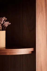 A modern shelf with a wooden shelving unit displaying a small vase with flowers, set against a dark wooden wall.