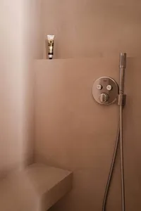 A minimalist bathroom with concrete walls, a hand shower, and a small bench.