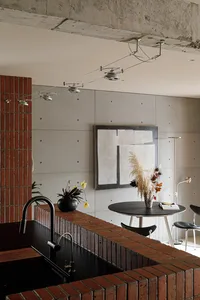 A minimalist kitchen with brick countertops and a concrete wall featuring modern track lighting and an abstract artwork.