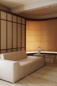 Modern minimalist living room with a white sofa on a textured rug, natural light filtering through sheer curtains, and a simp