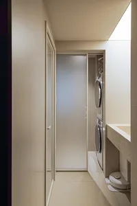 A minimalist modern bathroom and laundry room with tiled walls, featuring a clear shower door and washing machines.