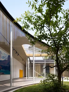 Modern building with glass walls, metal accents, and a tree in the foreground.