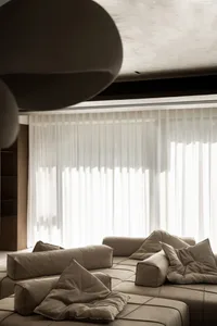 A modern interior design living room with a large window, white curtains, and a plush, beige sectional sofa adorned with cush