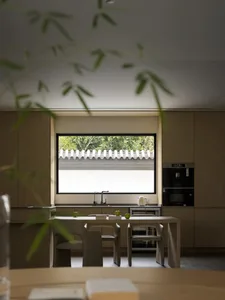 Modern kitchen with wooden cabinets, table, and chairs under a large window overlooking greenery.