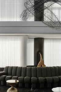 A modern living room featuring a black leather sofa, a sleek side table with a golden statue, and large windows with white bl