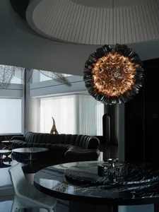A modern living room featuring a black leather sofa, a round marble table, and a unique chandelier.