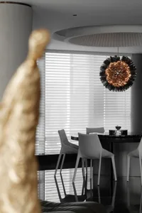A modern minimalist dining room with a metallic chandelier hanging above a round table surrounded by white chairs.