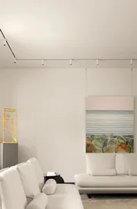 A modern minimalist living room with white sofas, textured fabric surfaces, and a geometric sculpture.