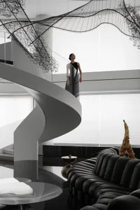 A modern residential living space featuring a sleek black spiral staircase with metal railings, glass panels, and stone accen