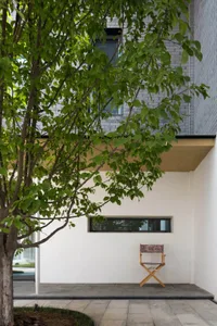 A minimalist modern building exterior made of concrete, featuring a tree and a director's chair.