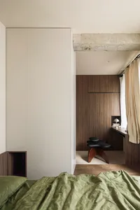 A minimalist bedroom featuring a wall cabinet with green bedding and a black stool.
