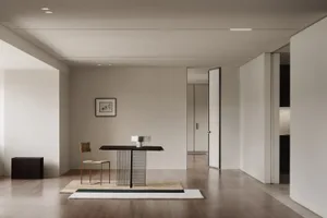 A minimalist interior featuring a metal console table with a black top, placed on a rug with green and beige tiles, next to a