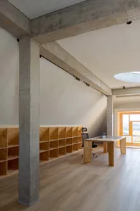 A minimalist office space featuring concrete walls and wooden furniture.