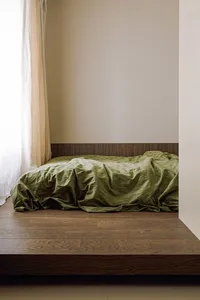 A modern bedroom featuring a wooden platform bed with a green bedspread.