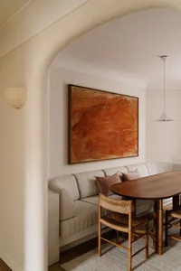 A modern interior design breakfast nook with a wooden table, white cushions, and a large abstract painting on the wall.