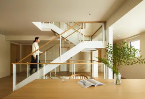 A modern living room featuring wooden and glass materials, with a person walking down a staircase in the background.