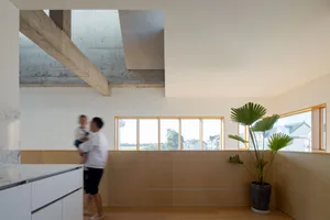 A modern residential apartment kitchen with a concrete ceiling beam, marble countertops, and large windows.