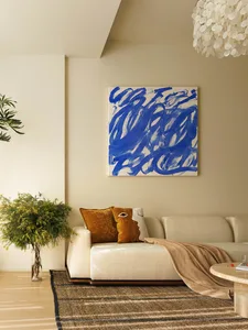 A minimalist living room featuring a white sofa with blue and white abstract art above, a wooden coffee table, and a woven ru