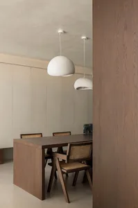 A modern dining room with wooden flooring, a wooden dining table, wooden chairs with wicker seats, and two white pendant ligh