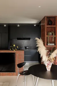 A modern kitchen with black cabinetry, white countertops, and exposed brick walls.