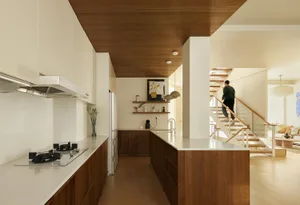 A modern kitchen with wooden cabinets, white countertops, and a stainless steel stove top oven.