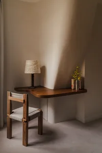 A modern home office setup featuring a wooden desk and chair, with a lamp and flowers on the desk.