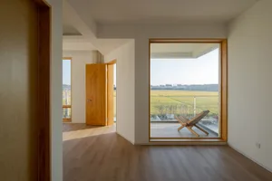A modern residential space featuring a large window overlooking a field, with a wooden floor and a wooden chair.