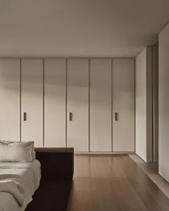 A minimalist bedroom featuring white paneling and wooden floors, with a sleek bed and minimalistic decor.