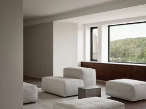 Modern minimalist living room with white sofas, large windows overlooking a forest.