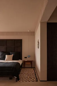 A minimalist bedroom featuring a bed with textured wooden headboard, a wooden nightstand, a wool rug with geometric patterns,
