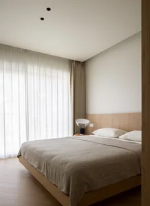 Modern minimalist bedroom with wooden furniture, white bedding, and sheer curtains.