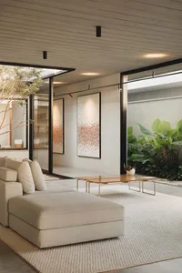 Modern minimalist living room with large canvases, concrete ceiling, and natural light from large glass doors leading to an o