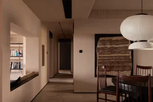 A minimalist residential dining room with a wooden dining table and chairs, a decorative wall hanging, and a hallway in the b