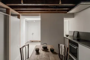 A minimalist residential kitchen with wooden table, concrete walls, and metal accents.