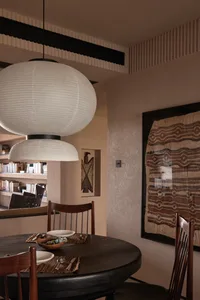 Modern dining room featuring a round wooden table with chairs, a pendant light fixture, and a framed textile artwork on the w