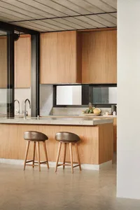 A modern kitchen with wooden cabinets and a concrete countertop, featuring a fruit bowl on the counter.