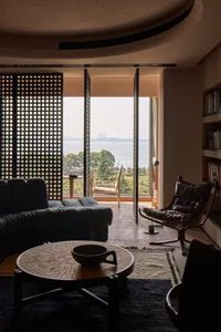 Modern living room with a leather sofa, round wooden table, and floor-to-ceiling view of the lake.