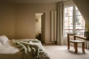 A minimalist bedroom with a bed covered in a green blanket and a white table with a vase of flowers.