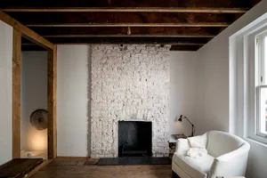 An industrial-style room with a white-brick fireplace, white armchair, and wooden floor.