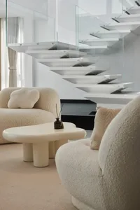 Modern living room with white fabric furniture, glass staircase, and white coffee table.