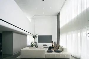 A modern minimalist living room with a white L-shaped sofa, large windows, and a large blank TV screen.