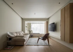 A modern living room with furniture and decor in neutral tones, featuring a couch, chair, and television.