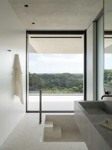 Modern minimalist bathroom featuring a stone bathtub with a concrete surround, large windows with a view of the forested hill