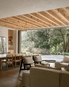 A minimalist living room featuring white concrete walls, large windows, and a comfortable seating area with light-colored fur
