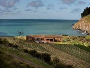 Modern house on beach with wooden exterior and corrugated metal roof.