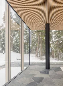 A modern interior design featuring wooden surfaces and large windows overlooking a snowy landscape.