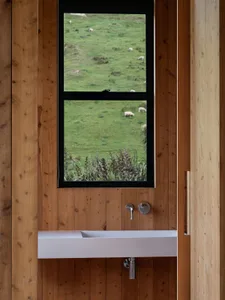 A modern bathroom with a view of a green landscape with sheep grazing.